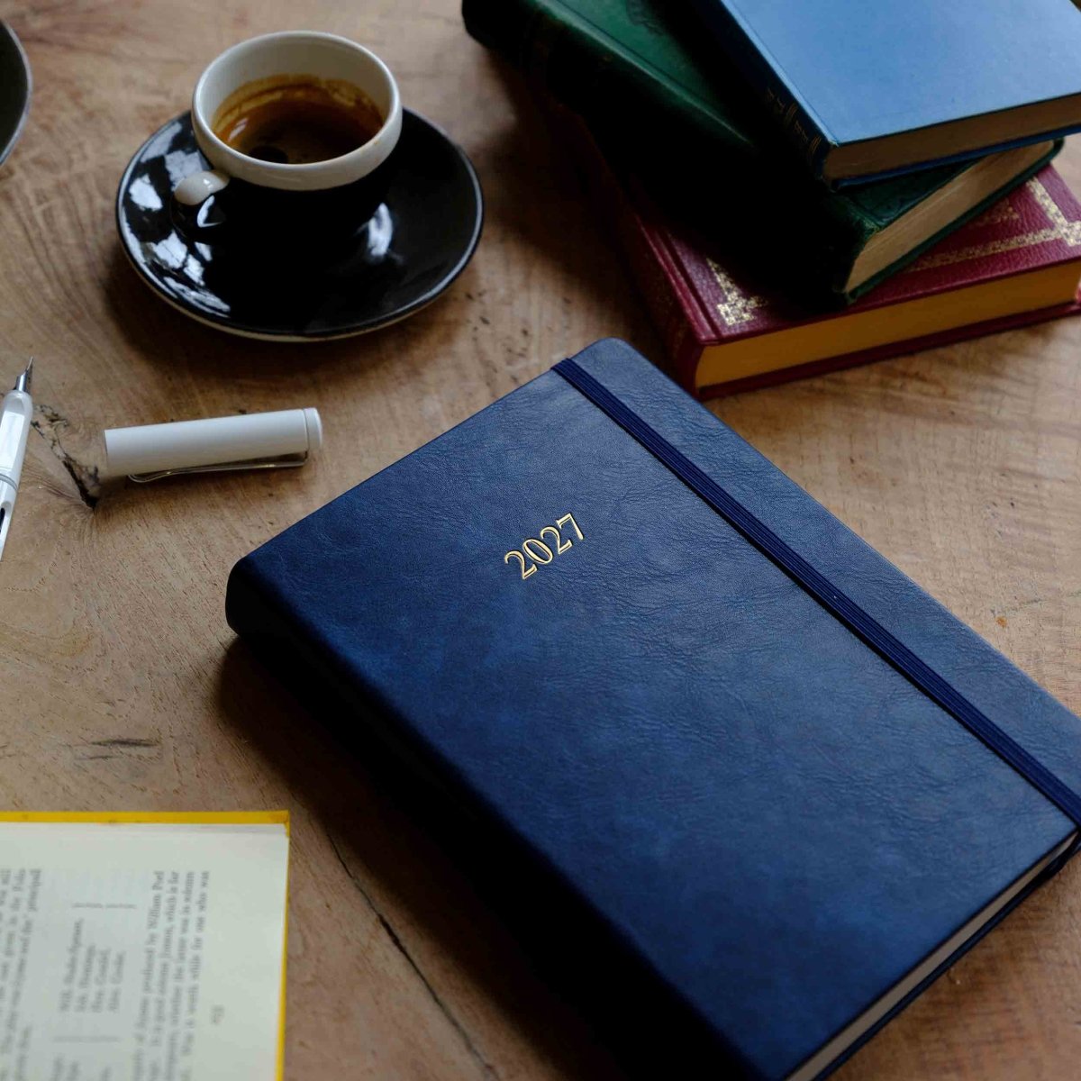 Blue 2027 journal with gold “2027” on cover, pen and cup on desk