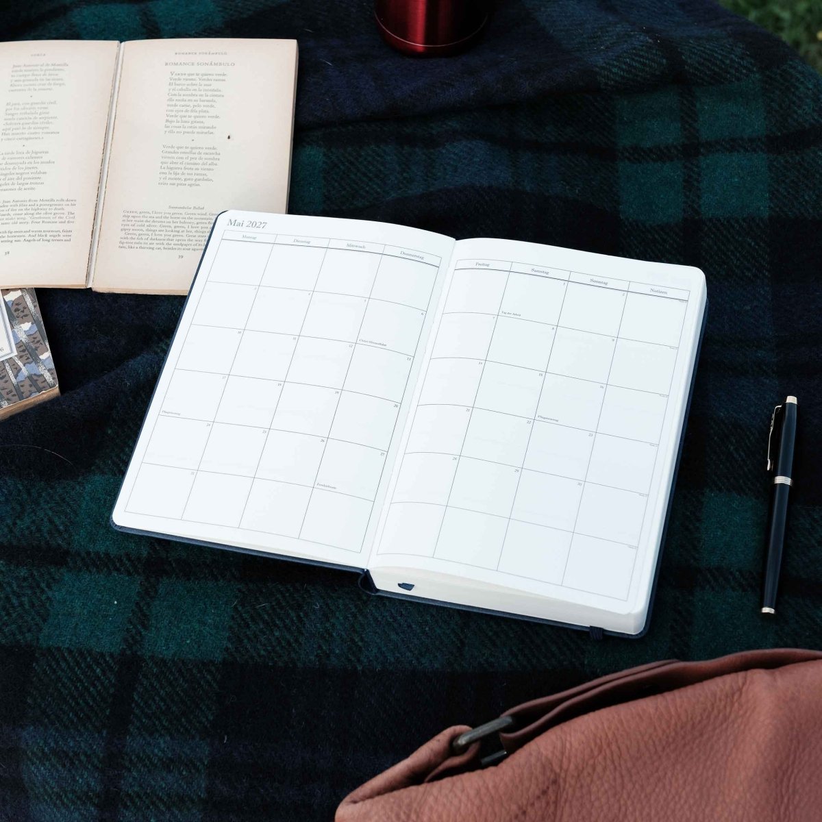 Open dark executive journal with calendar grid and lined pages, with pen
