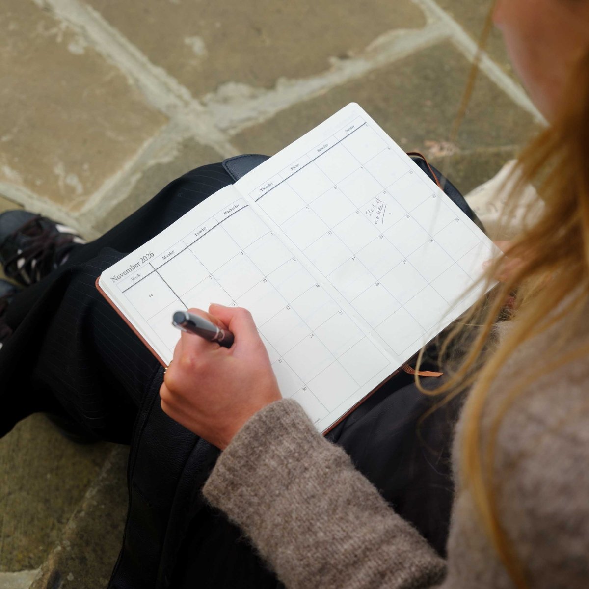Black desk journal opened to a weekly grid, with writing in progress